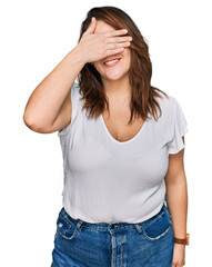 Fototapeta premium Young plus size woman wearing casual white t shirt smiling and laughing with hand on face covering eyes for surprise. blind concept.