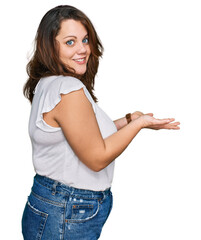 Young plus size woman wearing casual white t shirt pointing aside with hands open palms showing copy space, presenting advertisement smiling excited happy