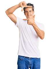 Fototapeta premium Young handsome man wearing casual white tshirt smiling making frame with hands and fingers with happy face. creativity and photography concept.