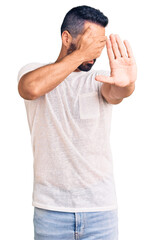 Young hispanic man wearing casual clothes covering eyes with hands and doing stop gesture with sad and fear expression. embarrassed and negative concept.