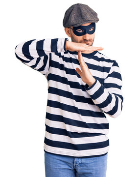 Young handsome man wearing burglar mask doing time out gesture with hands, frustrated and serious face