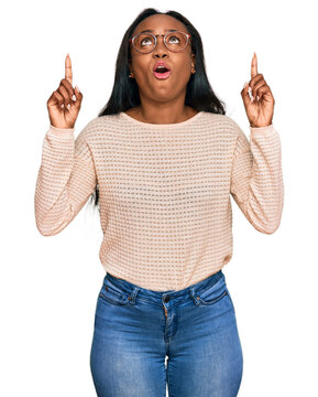 Young Black Woman Wearing Casual Clothes And Glasses Amazed And Surprised Looking Up And Pointing With Fingers And Raised Arms.