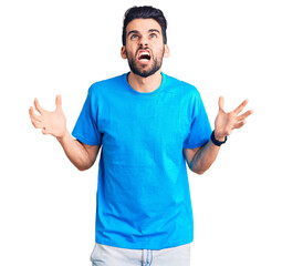 Fototapeta premium Young handsome man with beard wearing casual t-shirt crazy and mad shouting and yelling with aggressive expression and arms raised. frustration concept.