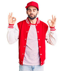 Young handsome man with beard wearing baseball jacket and cap relax and smiling with eyes closed doing meditation gesture with fingers. yoga concept.