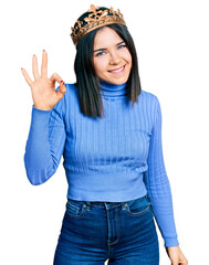 Young brunette woman with blue eyes wearing princess crown smiling positive doing ok sign with hand and fingers. successful expression.