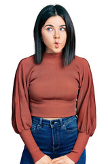 Young brunette woman with blue eyes wearing elegant sweater making fish face with lips, crazy and comical gesture. funny expression.