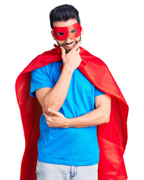 Young handsome man with beard wearing super hero costume looking confident at the camera smiling with crossed arms and hand raised on chin. thinking positive.