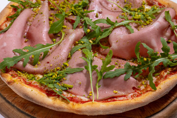 Pizza with ham, arugula and pistachios served on wooden platter