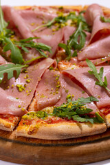 Pizza with ham, arugula and pistachios served on wooden platter