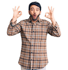 Young hispanic man wearing casual clothes looking surprised and shocked doing ok approval symbol with fingers. crazy expression