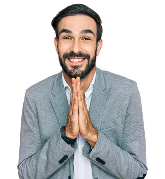 Young hispanic man wearing business clothes praying with hands together asking for forgiveness smiling confident.