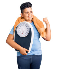Little boy kid holding weight machine to balance weight loss pointing thumb up to the side smiling...