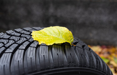 Detail of a wet yellow leaf on a winter tyre as a symbol that the time has come to change tyres in autumn. Driving safety, road safety and car service concept.