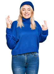 Fototapeta na wymiar Young caucasian woman wearing wool winter sweater and cap gesturing finger crossed smiling with hope and eyes closed. luck and superstitious concept.