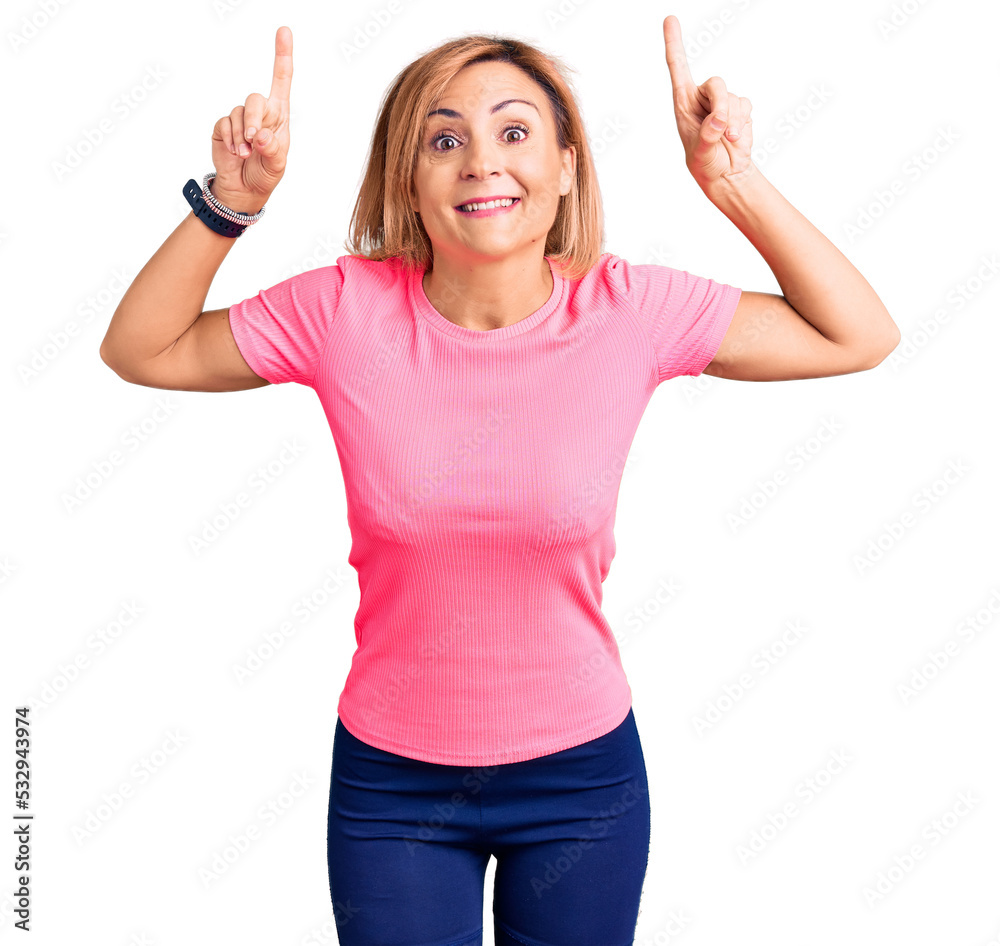 Wall mural young blonde woman wearing sportswear smiling amazed and surprised and pointing up with fingers and 