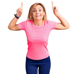 Young blonde woman wearing sportswear smiling amazed and surprised and pointing up with fingers and raised arms.