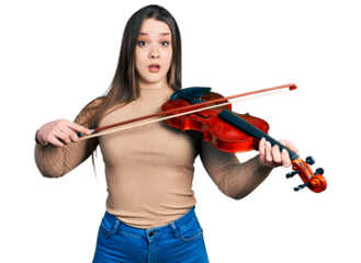 Young hispanic girl playing violin in shock face, looking skeptical and sarcastic, surprised with open mouth
