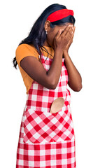 Young indian girl wearing professional baker apron with sad expression covering face with hands while crying. depression concept.