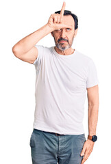 Middle age handsome man wearing casual t-shirt making fun of people with fingers on forehead doing loser gesture mocking and insulting.