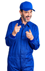 Middle age handsome man wearing mechanic uniform pointing fingers to camera with happy and funny...