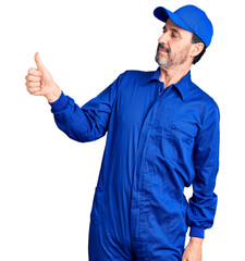 Middle age handsome man wearing mechanic uniform looking proud, smiling doing thumbs up gesture to...