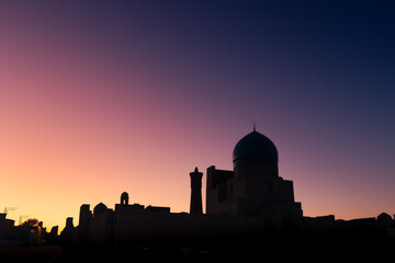 Rooftop silhouette with old mosque big dome against colorful sunset sky, Bukhara, Uzbekistan