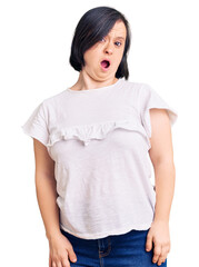 Fototapeta premium Brunette woman with down syndrome wearing casual white tshirt in shock face, looking skeptical and sarcastic, surprised with open mouth