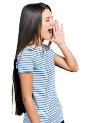 Fototapeta premium Young brunette girl with long hair wearing casual striped t shirt shouting and screaming loud to side with hand on mouth. communication concept.