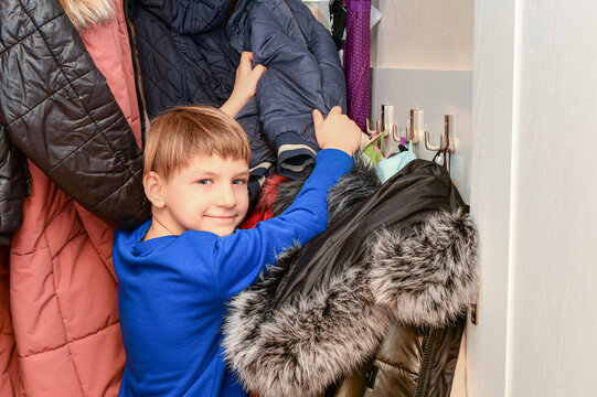 The boy is looking for his winter things in his home wardrobe before going outside.
