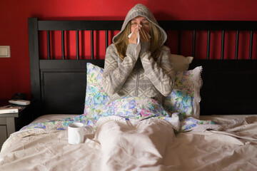 woman with a cold in her bed blows her nose with a tissue