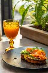 sandwich with salmon and avocado on a black plate with a glass of juice