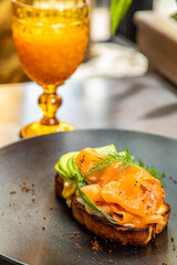 sandwich with salmon and avocado on a black plate with a glass of juice