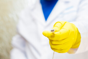 A doctor in a medical gown and protective gloves holds a usb type c cable in his hand. The face is not visible.