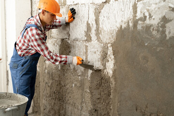 Construction worker plasterer with trowel plastering wall cement mortar for work. Renovation at home