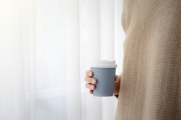 Fototapeta na wymiar closeup woman hand holding paper cup of hot coffee with semi transparent white curtain