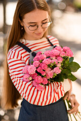 bunch of bright pink roses neatly holds young attractive woman and look at it