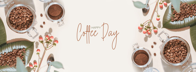 Fototapeta Coffee Day holiday banner with organic roasted coffee beans on a green leaves and coffee powder in a glass jar on an ivory background with shadows and congratulation inscription. Flat lay, Banner size obraz