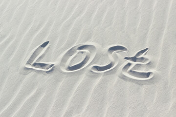 lost written with finger on white sand, concept of missing and asking for help, word on sand