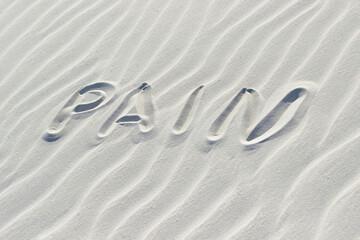 pain is written with a finger on white sand, the concept of illness and emotional state, the word on the sand