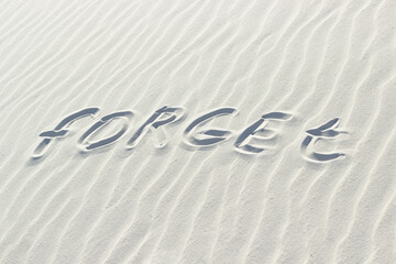 Fototapeta na wymiar forget written with finger on white sand. bad memory concept, word on sand