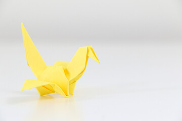 Yellow Japanese origami crane on left of white background