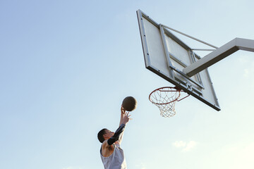 Low angle of basketball player jumping and throwing ball into basket hoop against blue sky 