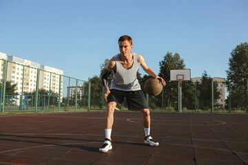 Obraz premium Full body of focused athletic man with basketball playing street ball on outdoors urban playground on sunny day in summer 