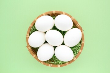 Fresh white chicken eggs in wooden rattan wicker basket on green background. Natural healthy nutrition organic farm food product concept. World egg day, easter holiday composition. Close-up, flatlay