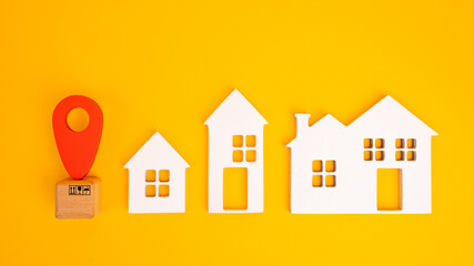 Cardboard boxes and a red position pin in city of white toy house on yellow background. Locating packages and goods.