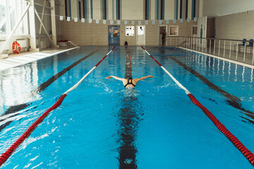 Back view of professional sportswoman showing Butterfly stroke and swimming in indoor pool during training  