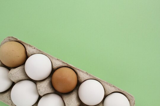 Fresh white and brown chicken eggs in carton paper box on green background. Natural healthy nutrition organic farm food product concept. World egg day, easter holiday composition. Copy space, flatlay