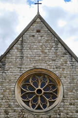 Close-up of the facade of early English style church with a rose window and brick wall against cloudy sky. 