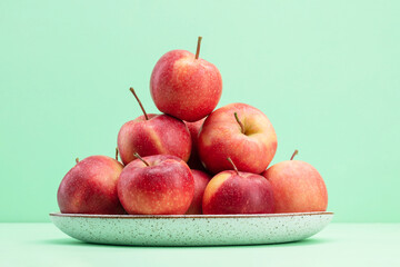 Red apples in a plate on a green background. Close-up of red royal gala apples. Heap of red...