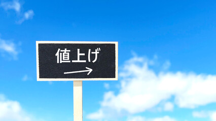 値上げの文字入り黒いプレート_青空背景_右空間